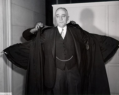 Justice John M. Harlan dons his robe before his Investiture with the gold watch chain clearly visible.